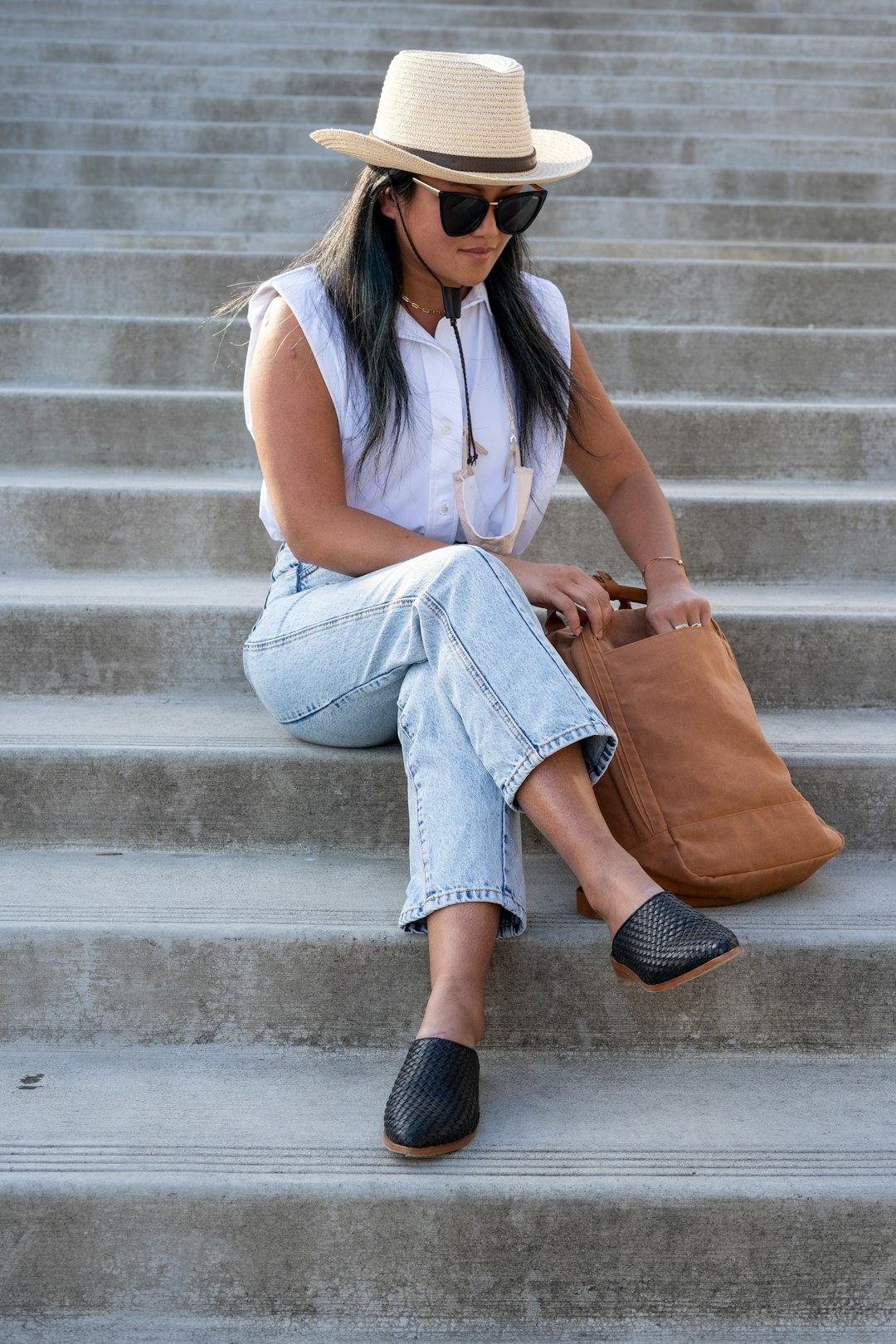 woman in white sleeveless shirt and blue denim shorts sitting on gray concrete stairs