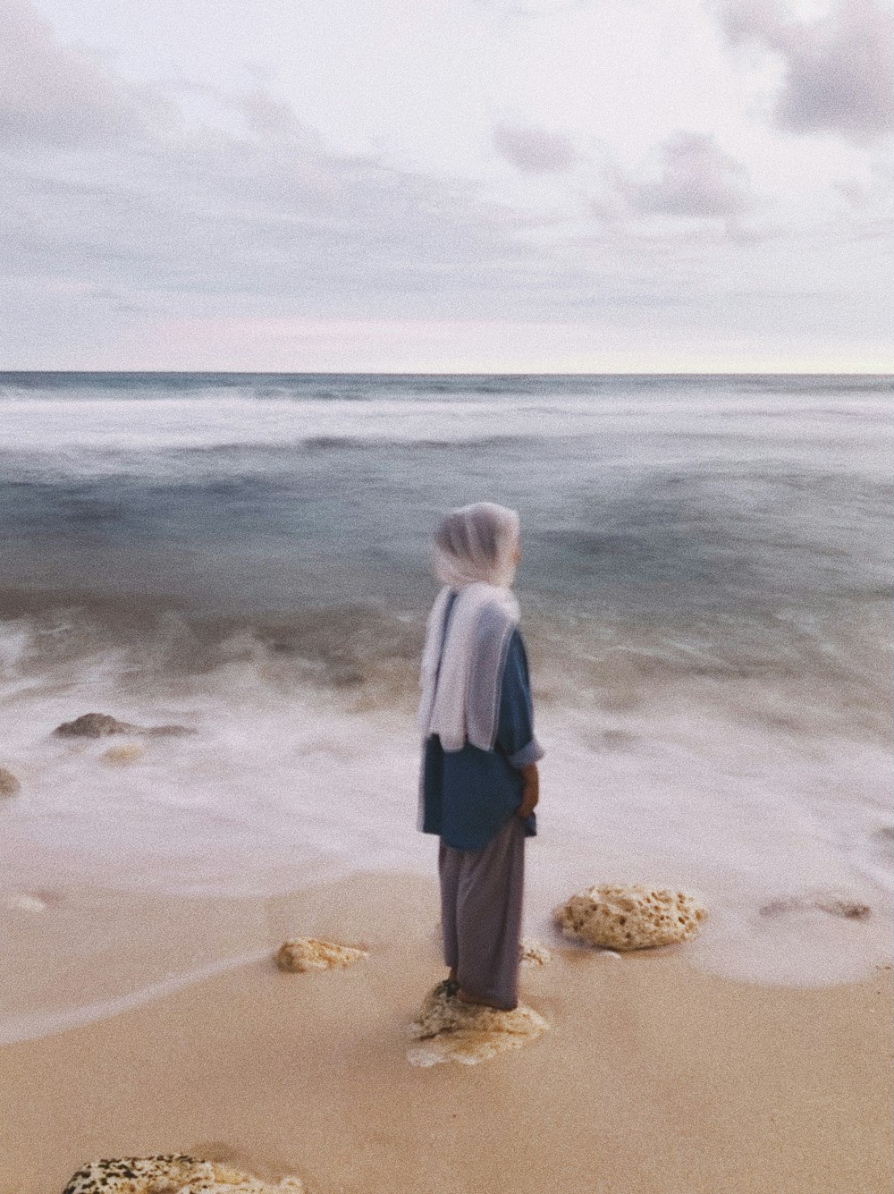 woman in gray long sleeve shirt and blue skirt standing on seashore during daytime