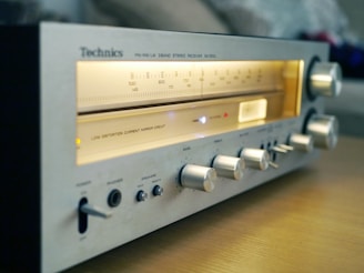 A vintage Technics stereo receiver with illuminated frequency dials and several knobs for adjustments, resting on a wooden surface.