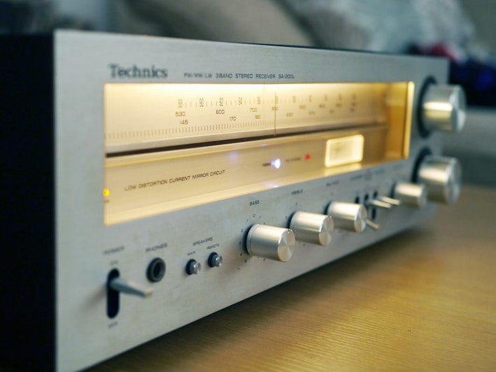 A vintage Technics stereo receiver with illuminated frequency dials and several knobs for adjustments, resting on a wooden surface.