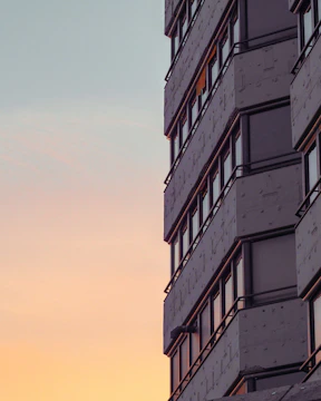 A sleek high-rise building with floor-to-ceiling windows showcasing the New York City skyline at sunset.