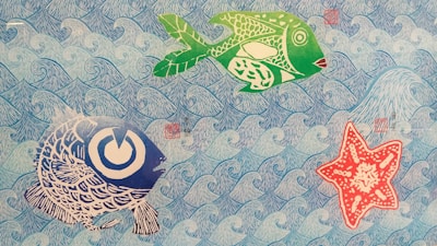 The image depicts a colorful and artistic underwater scene. There are two stylized fish and one starfish against a background of repeating blue waves. The fish are rendered in green and large stripes of blue with intricate patterns, while the starfish is red with white patterns. The overall style is illustrative and playful.