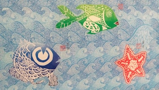 The image depicts a colorful and artistic underwater scene. There are two stylized fish and one starfish against a background of repeating blue waves. The fish are rendered in green and large stripes of blue with intricate patterns, while the starfish is red with white patterns. The overall style is illustrative and playful.