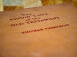 A close-up of a book cover with red text reading 'The Kindly Laws of the Old Testament' by Thomas Cameron, set against a textured, orange-brown background.