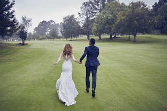man and woman in wedding dress walking on green grass field during daytime
