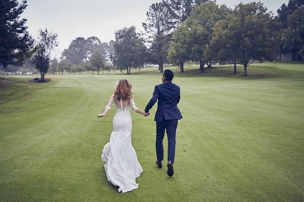 man and woman in wedding dress walking on green grass field during daytime
