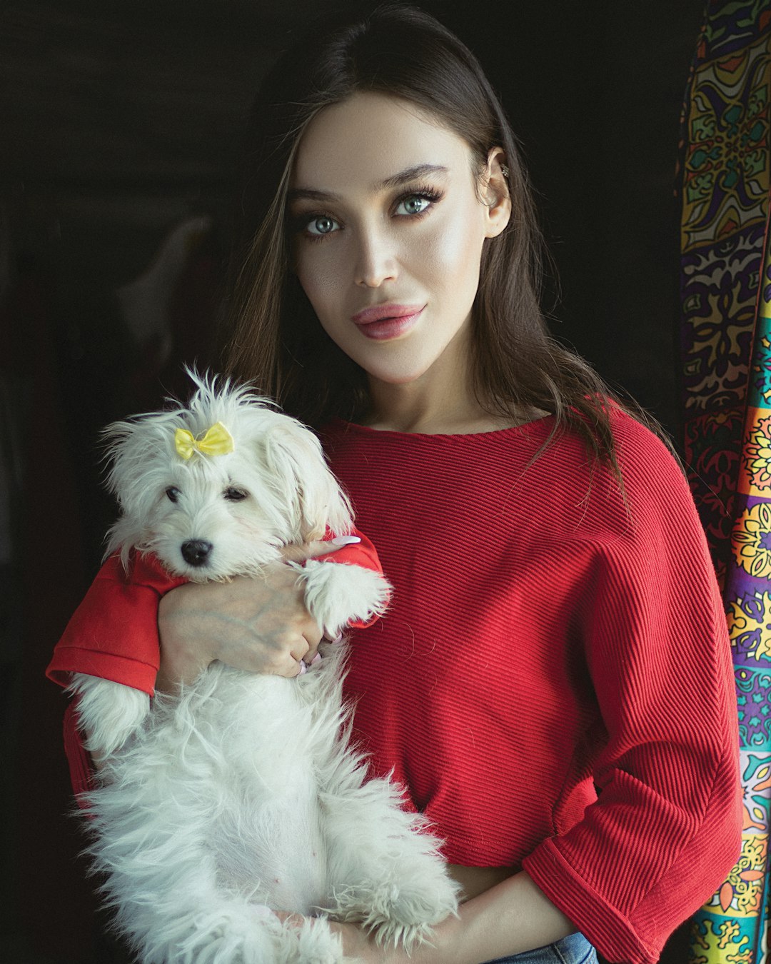 woman in red long sleeve shirt holding white long coated small dog