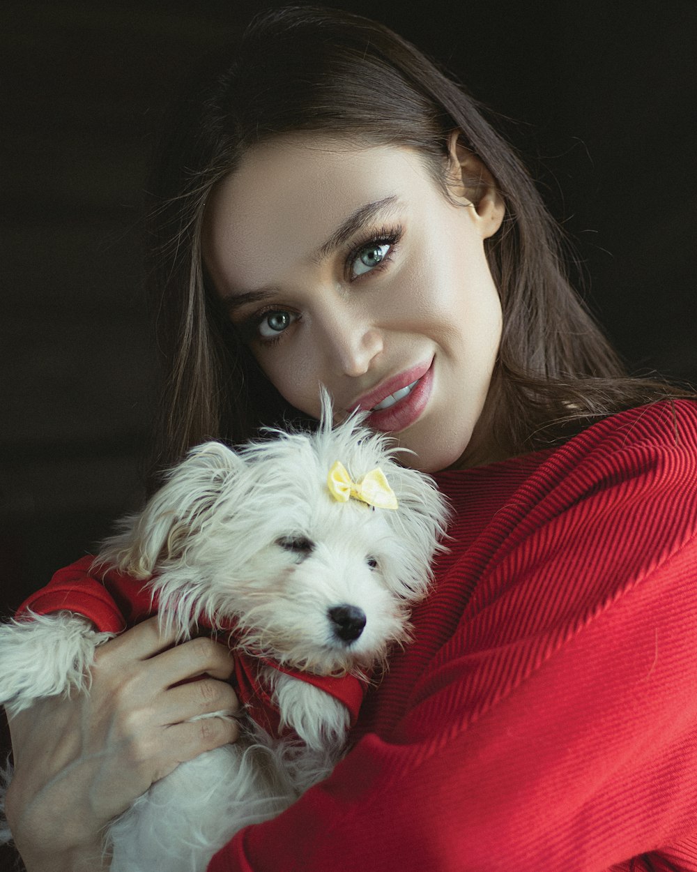 woman in red long sleeve shirt holding white long coated small dog