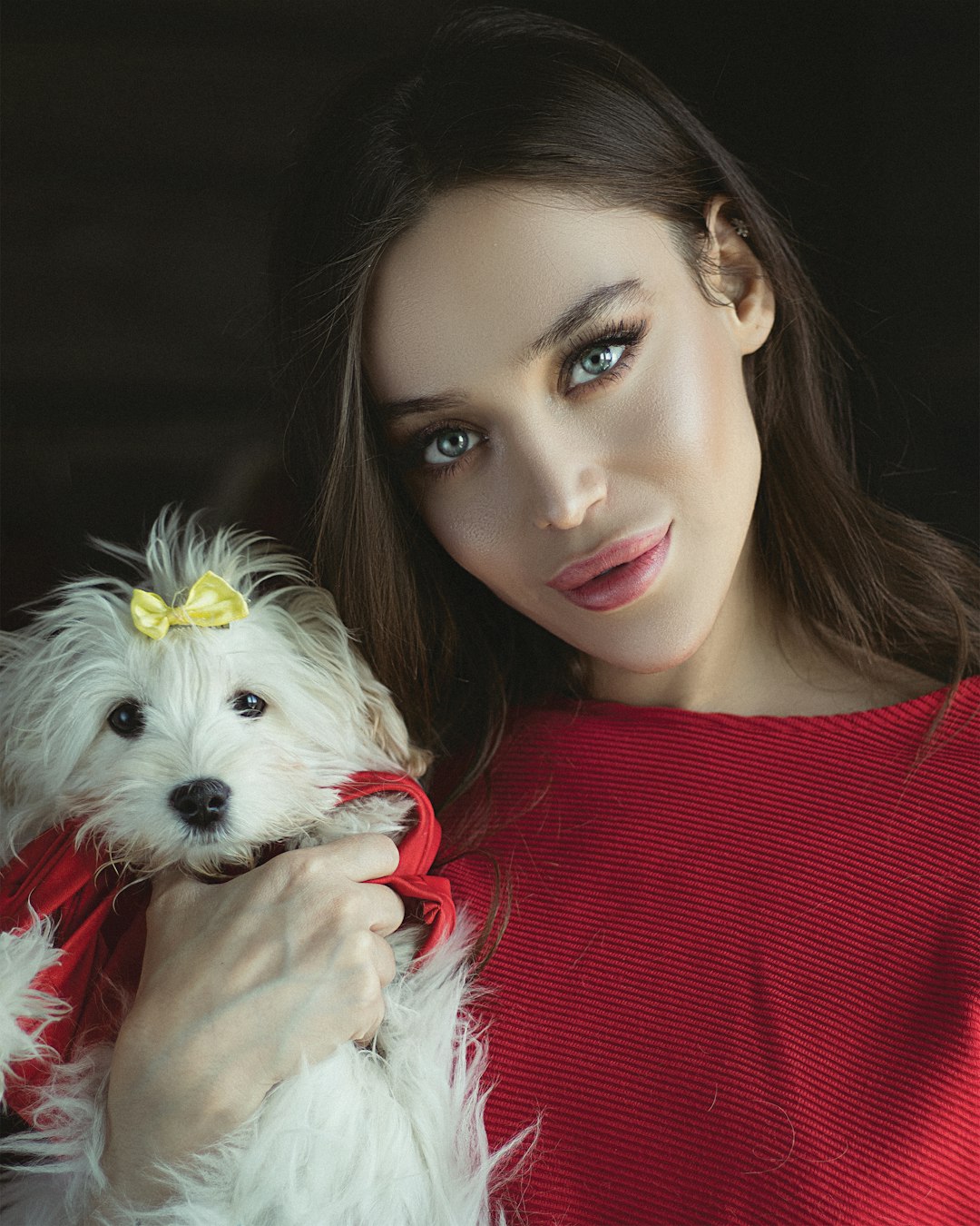 woman in red turtleneck sweater holding white long coated small dog