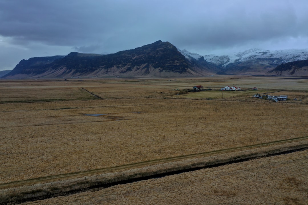 green grass field near mountain under white clouds during daytime