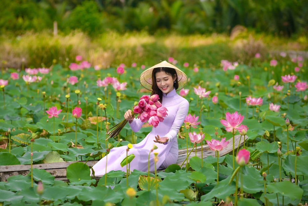 woman in white long sleeve dress and brown sun hat holding pink flowers