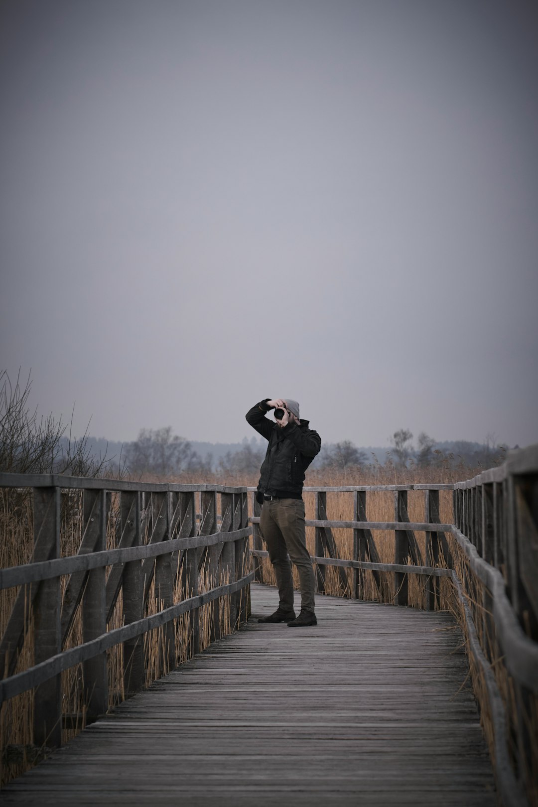 man in black jacket and brown pants standing on brown wooden bridge