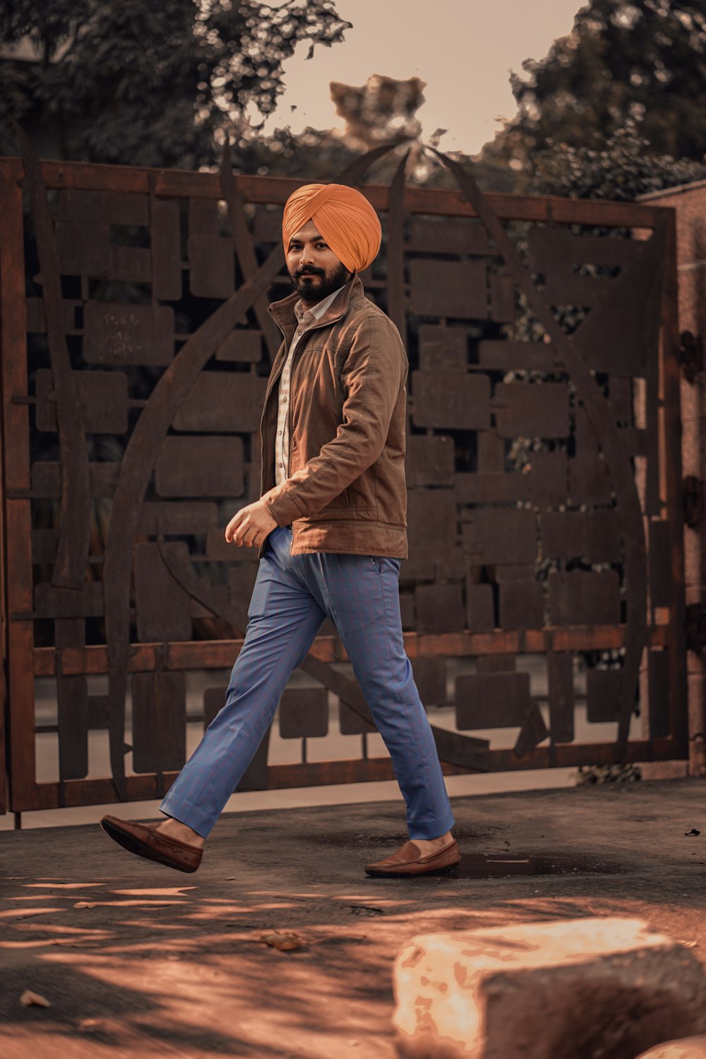 Hombre con chaqueta marrón y jeans de mezclilla azul de pie en piso de madera marrón