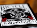 A close-up of a playing card box labeled Black Tiger Deck, featuring bold text and intricate design elements with a focus on a monochrome tiger illustration. Red decorative accents frame the corners while the overall color scheme is black and white.