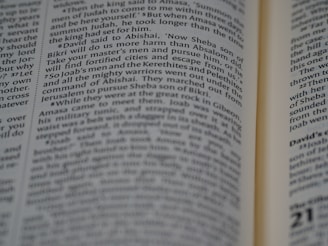 A close-up view of an open book with text focusing on biblical scripture. The text is printed in two columns on a thin, slightly yellowed page, indicating an older or traditional style publication. The lighting highlights parts of the text while leaving other areas slightly shadowed.