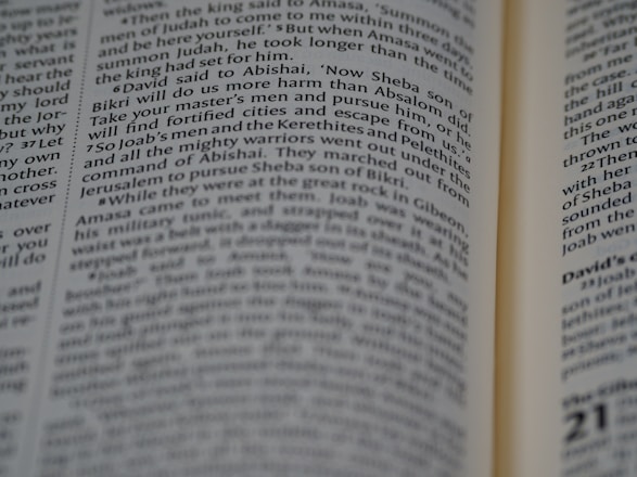 A close-up view of an open book with text focusing on biblical scripture. The text is printed in two columns on a thin, slightly yellowed page, indicating an older or traditional style publication. The lighting highlights parts of the text while leaving other areas slightly shadowed.