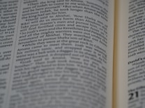 A close-up view of an open book with text focusing on biblical scripture. The text is printed in two columns on a thin, slightly yellowed page, indicating an older or traditional style publication. The lighting highlights parts of the text while leaving other areas slightly shadowed.