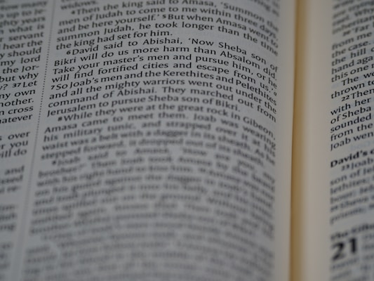 A close-up view of an open book with text focusing on biblical scripture. The text is printed in two columns on a thin, slightly yellowed page, indicating an older or traditional style publication. The lighting highlights parts of the text while leaving other areas slightly shadowed.