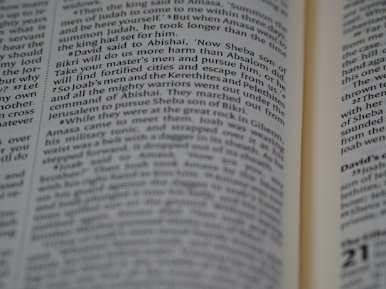 A close-up view of an open book with text focusing on biblical scripture. The text is printed in two columns on a thin, slightly yellowed page, indicating an older or traditional style publication. The lighting highlights parts of the text while leaving other areas slightly shadowed.