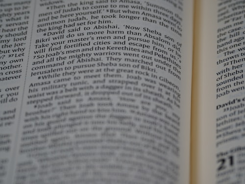 A close-up view of an open book with text focusing on biblical scripture. The text is printed in two columns on a thin, slightly yellowed page, indicating an older or traditional style publication. The lighting highlights parts of the text while leaving other areas slightly shadowed.