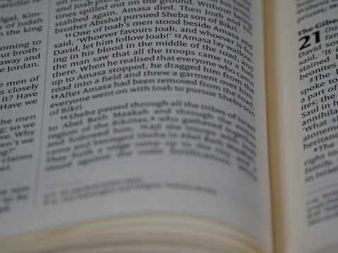 A close-up view of an open book with focused text on a page. The text is in a column format, typical of a printed book. Some parts of the text are blurry, possibly due to shallow depth of field.