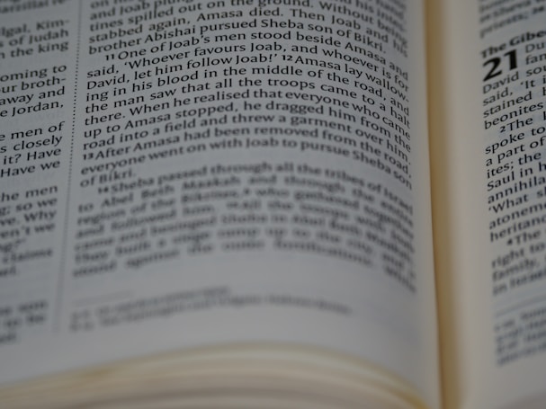 A close-up view of an open book with focused text on a page. The text is in a column format, typical of a printed book. Some parts of the text are blurry, possibly due to shallow depth of field.