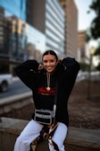 man in black hoodie and black and white pants sitting on concrete bench during daytime