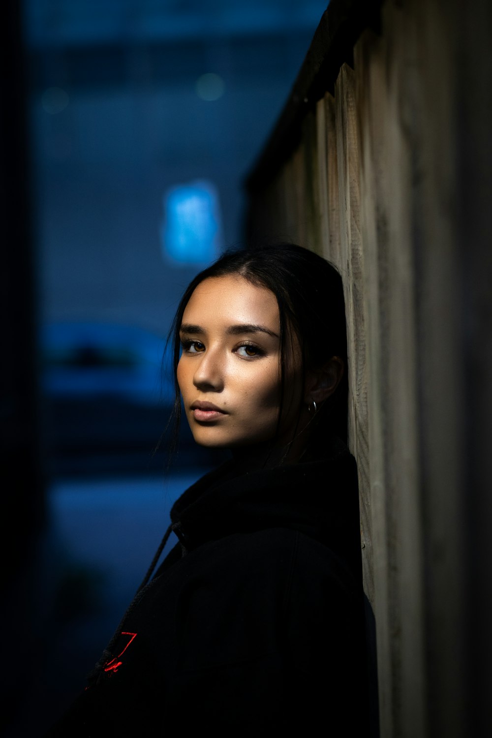 woman in black hoodie standing near brown wall