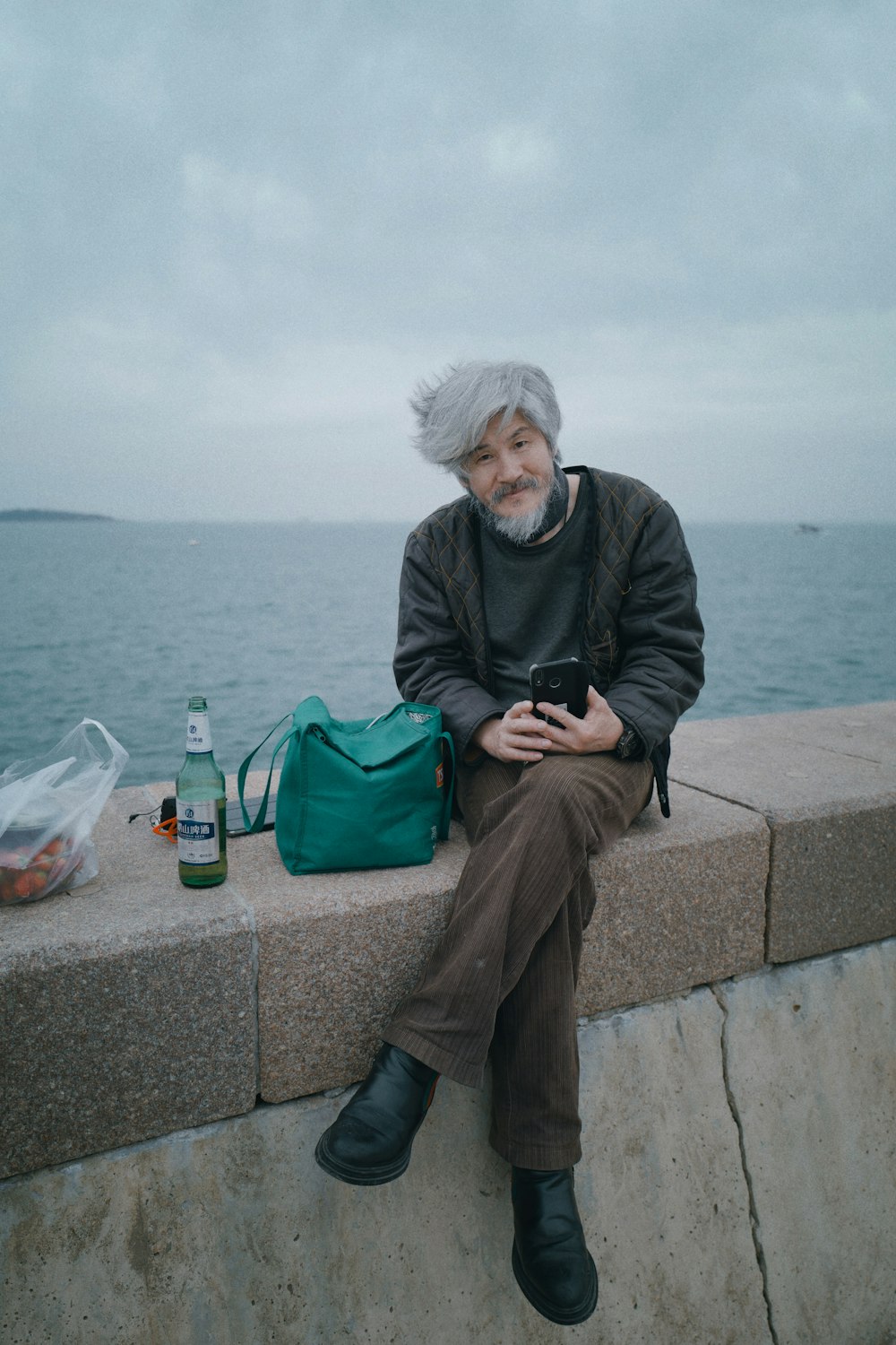 man in black jacket and brown pants sitting on concrete bench