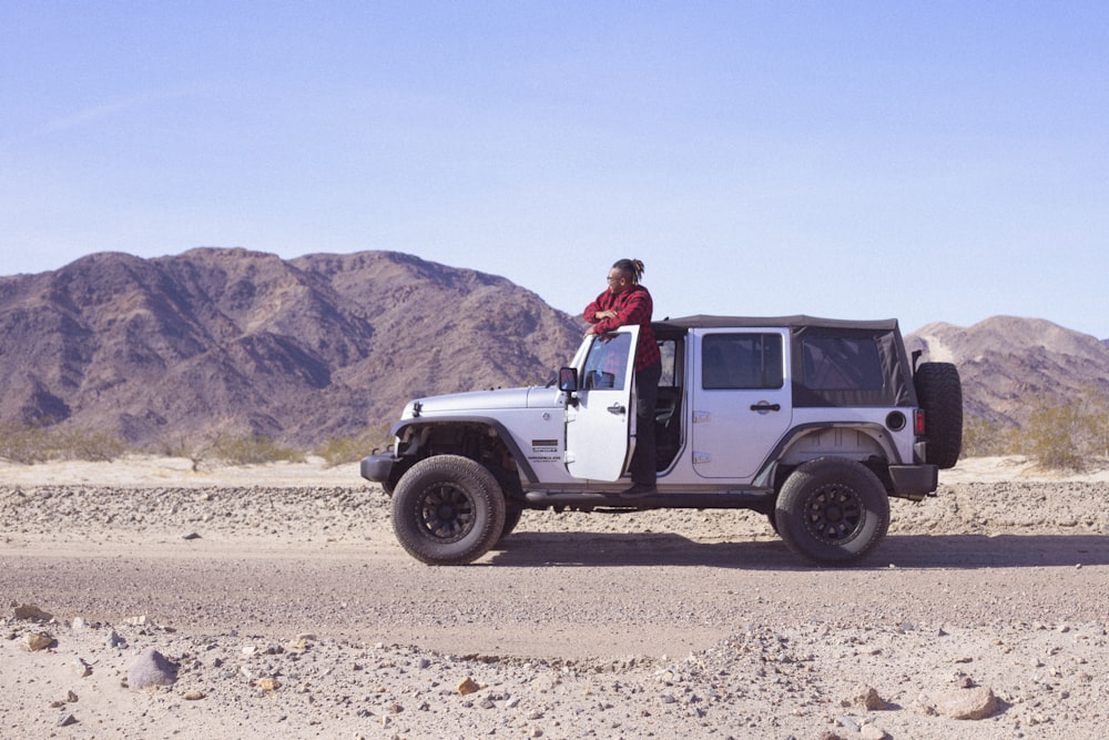 man in red shirt standing beside white suv during daytime