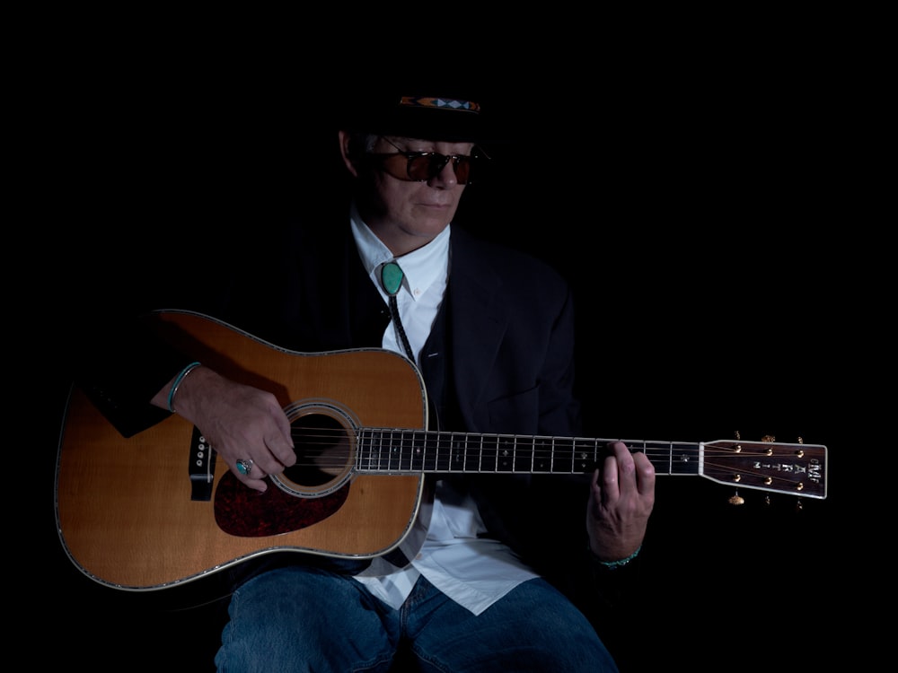 Hombre con traje negro tocando la guitarra acústica marrón