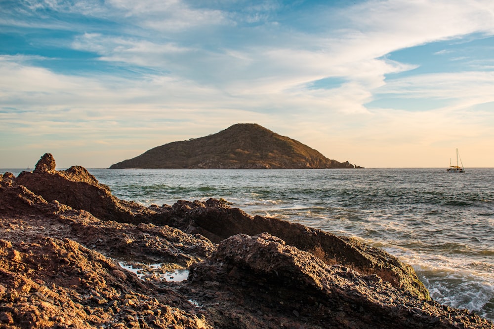 brown rocky mountain beside sea under blue sky during daytime