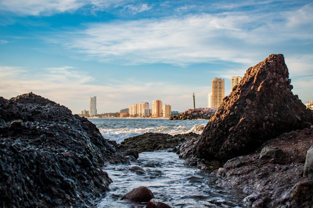 rocky shore with water waves near city buildings during daytime