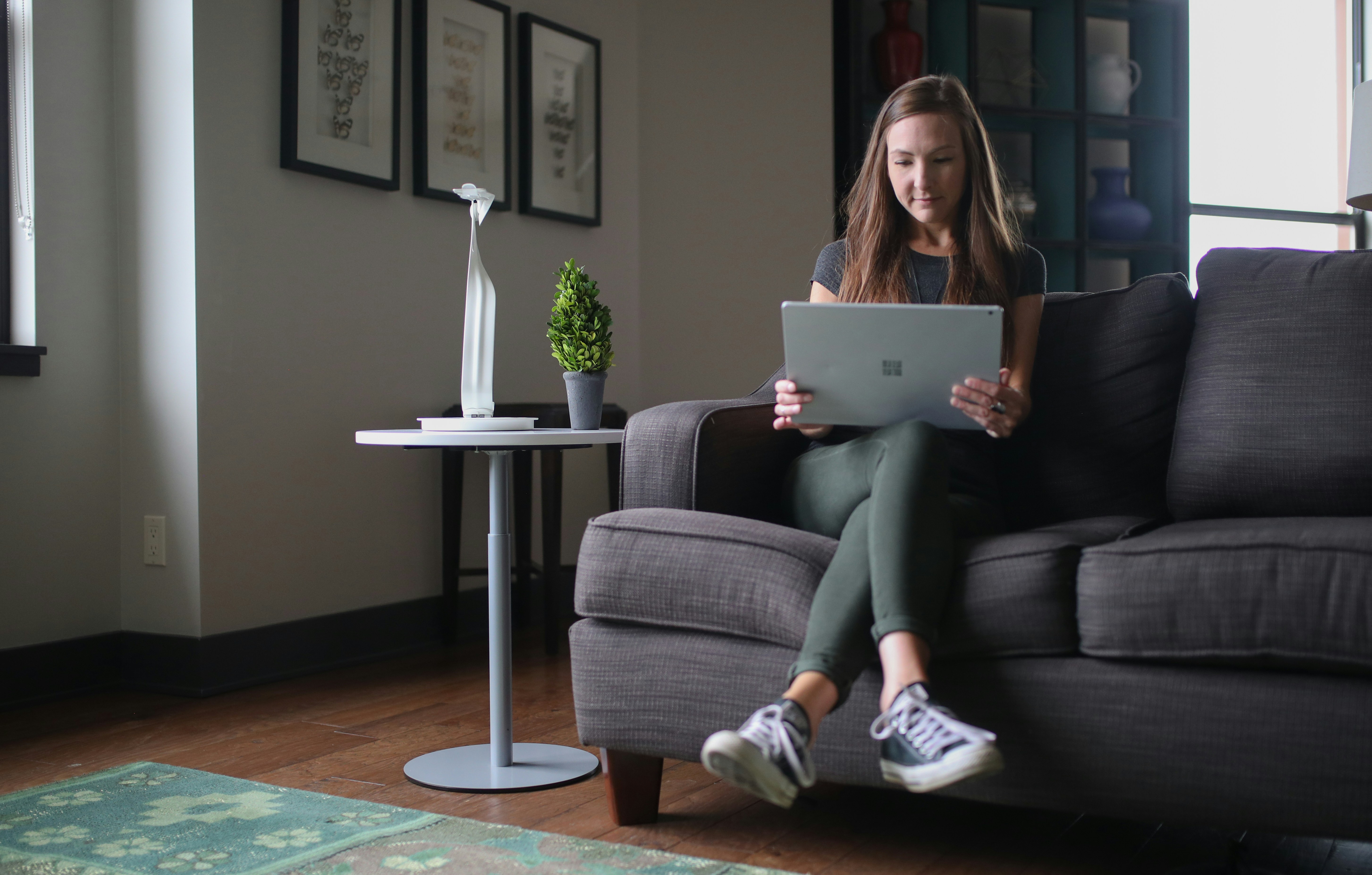 woman in blue tank top sitting on gray sofa using macbook