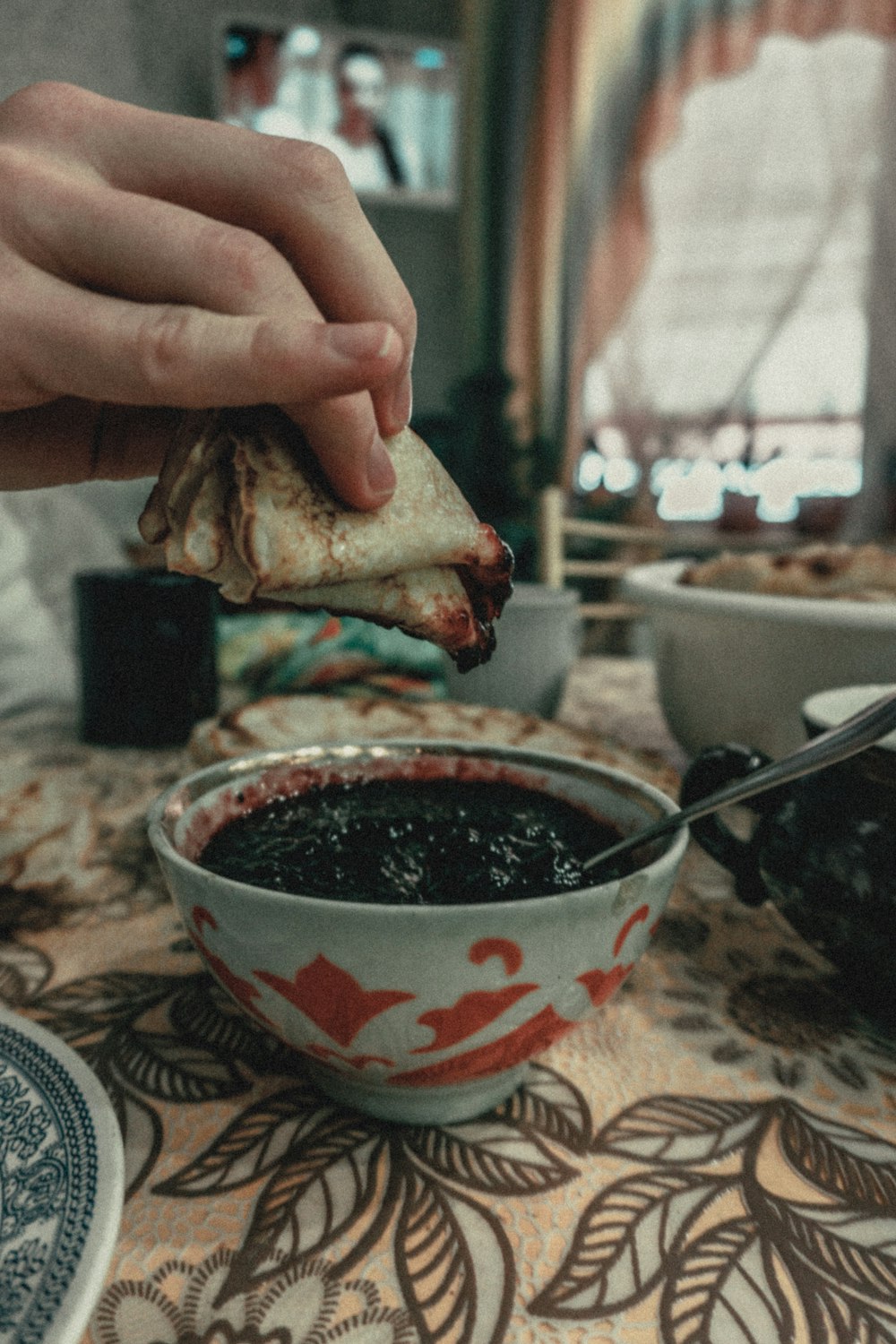 person holding bread near red and white ceramic bowl