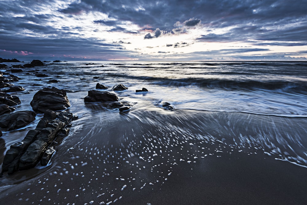 ocean waves crashing on rocks under cloudy sky during daytime