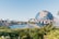 A large globe with the word 'Universal' prominently displayed in front. Lush greenery and palm trees surround the area, with a body of water and various buildings in the background, suggesting an amusement park setting. The sky is clear and bright, contributing to a lively atmosphere.