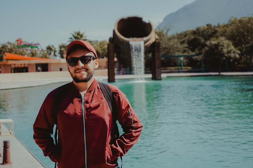 man in red zip up jacket standing near body of water during daytime