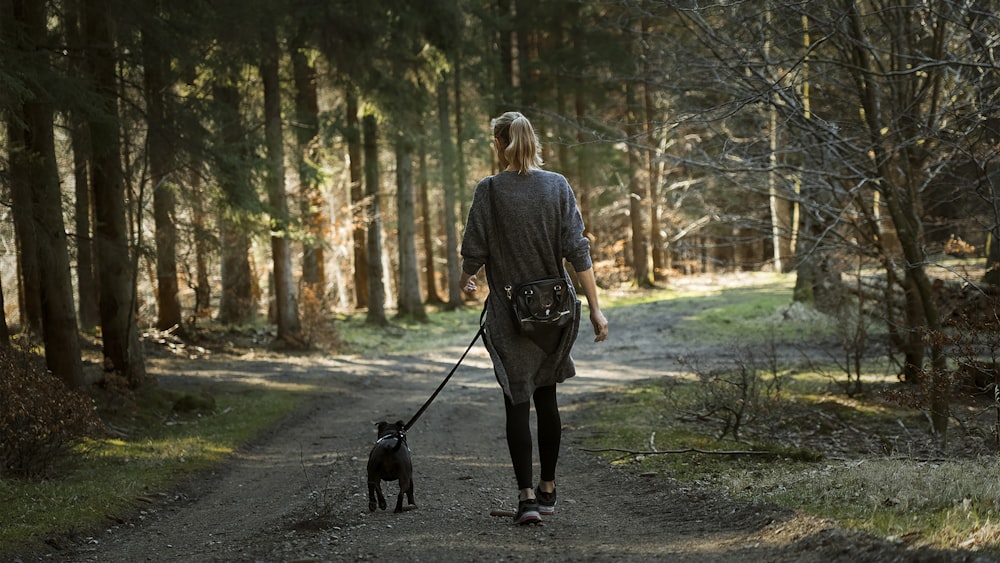 woman in black jacket walking with black labrador retriever on pathway during daytime