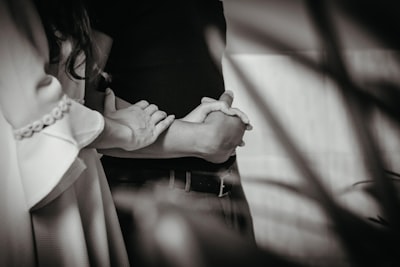 grayscale photo of woman in white long sleeve shirt holding mans hand faithful zoom background