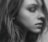 A close-up black and white portrait of a person looking to the side, with hair falling naturally around the face. The lighting highlights the contours and textures of the skin and hair, creating a soft and detailed visual effect.