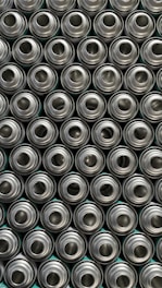 A pattern of tightly packed, identical, metallic aluminum cans viewed from above, displaying their circular openings.