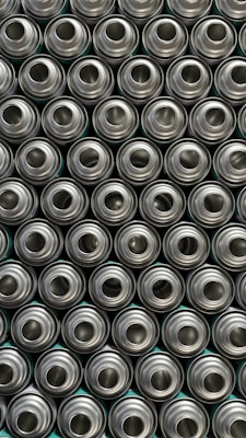 A pattern of tightly packed, identical, metallic aluminum cans viewed from above, displaying their circular openings.
