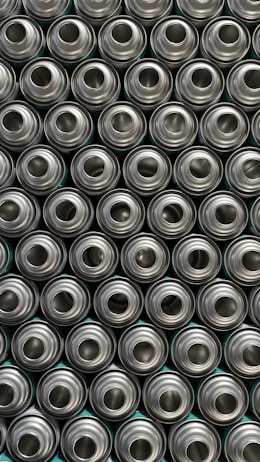 A pattern of tightly packed, identical, metallic aluminum cans viewed from above, displaying their circular openings.