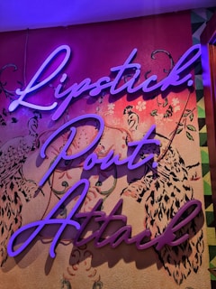 Neon-style cursive text spelling 'Lipstick. Pout. Attack.' is displayed against a decorative wallpaper background featuring intricate floral and bird patterns in contrasting colors.