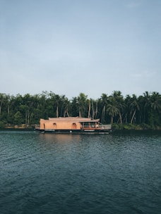A serene houseboat floating gently on calm waters at sunset, surrounded by lush greenery.