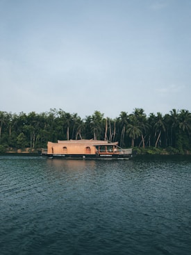 A traditional houseboat floats on a calm river with lush greenery and dense forest trees in the background, creating a peaceful and serene setting.