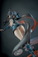 A dynamic perspective of an anime-style figurine featuring a character with long dark hair, dressed in a blue outfit with flowing elements. The figure is posed dramatically, with movement implied by the sweeping motion of the costume.