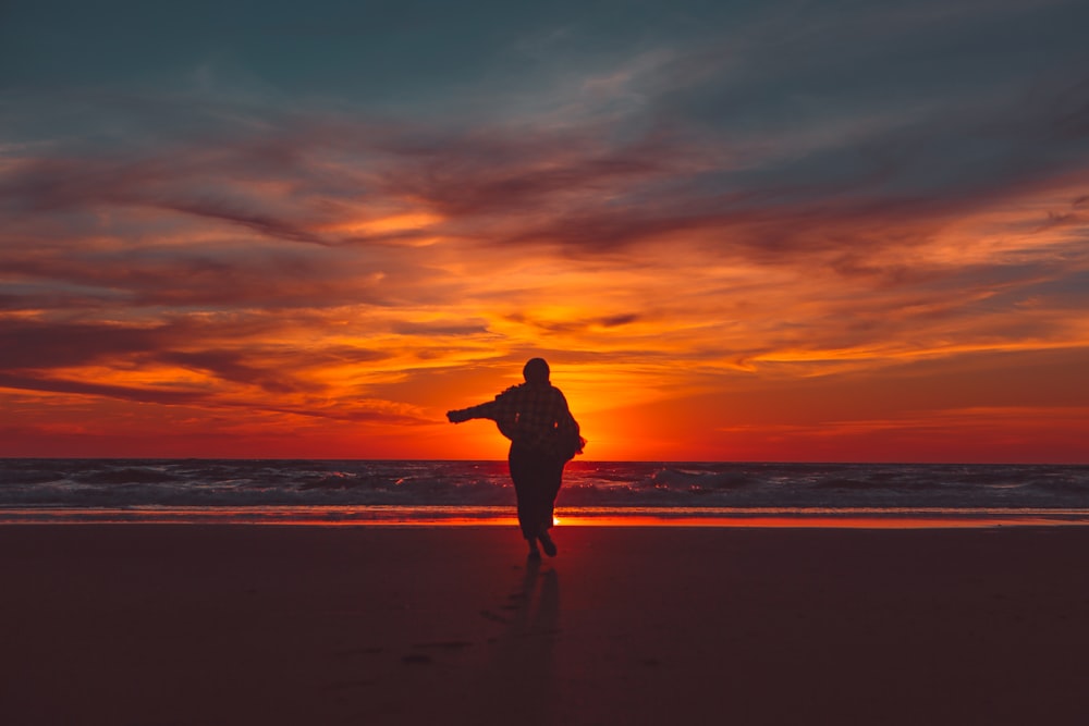 Silueta del hombre de pie en la playa durante la puesta del sol