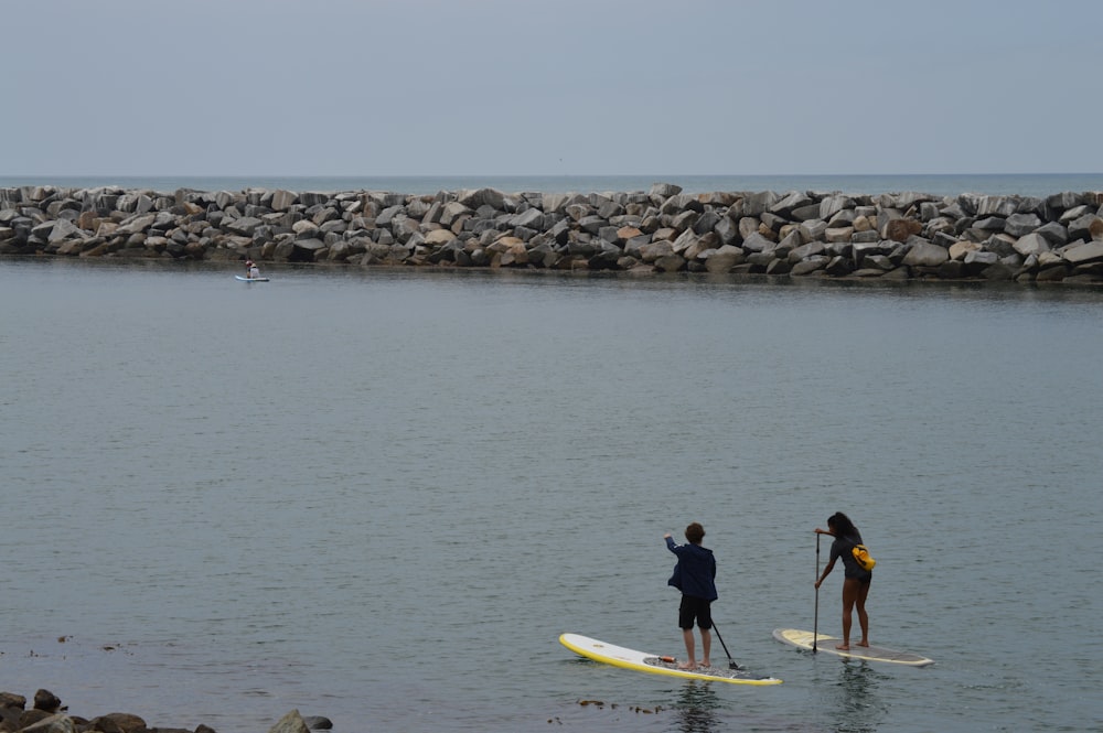 uomo e donna in muta nera che cavalcano una tavola da surf gialla sullo specchio d'acqua durante il giorno